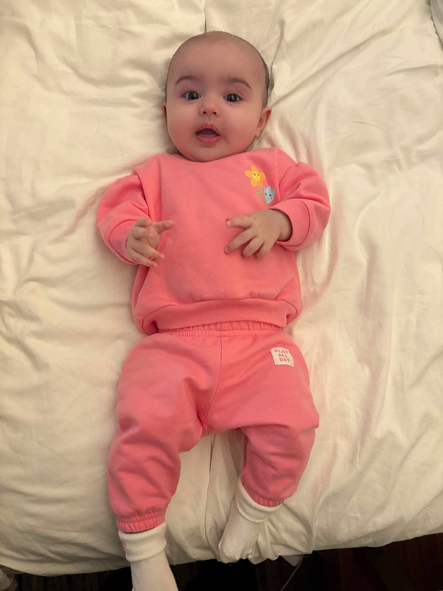 Layla Wright joined the competition — help win amazing prizes! baby, bed, child, comfortable, cozy, cute, expression, face, indoors, infant, lying_down, person, pink_clothing, portrait, sleepwear, small_hands, socks, soft_lighting, white_bed_sheet, young