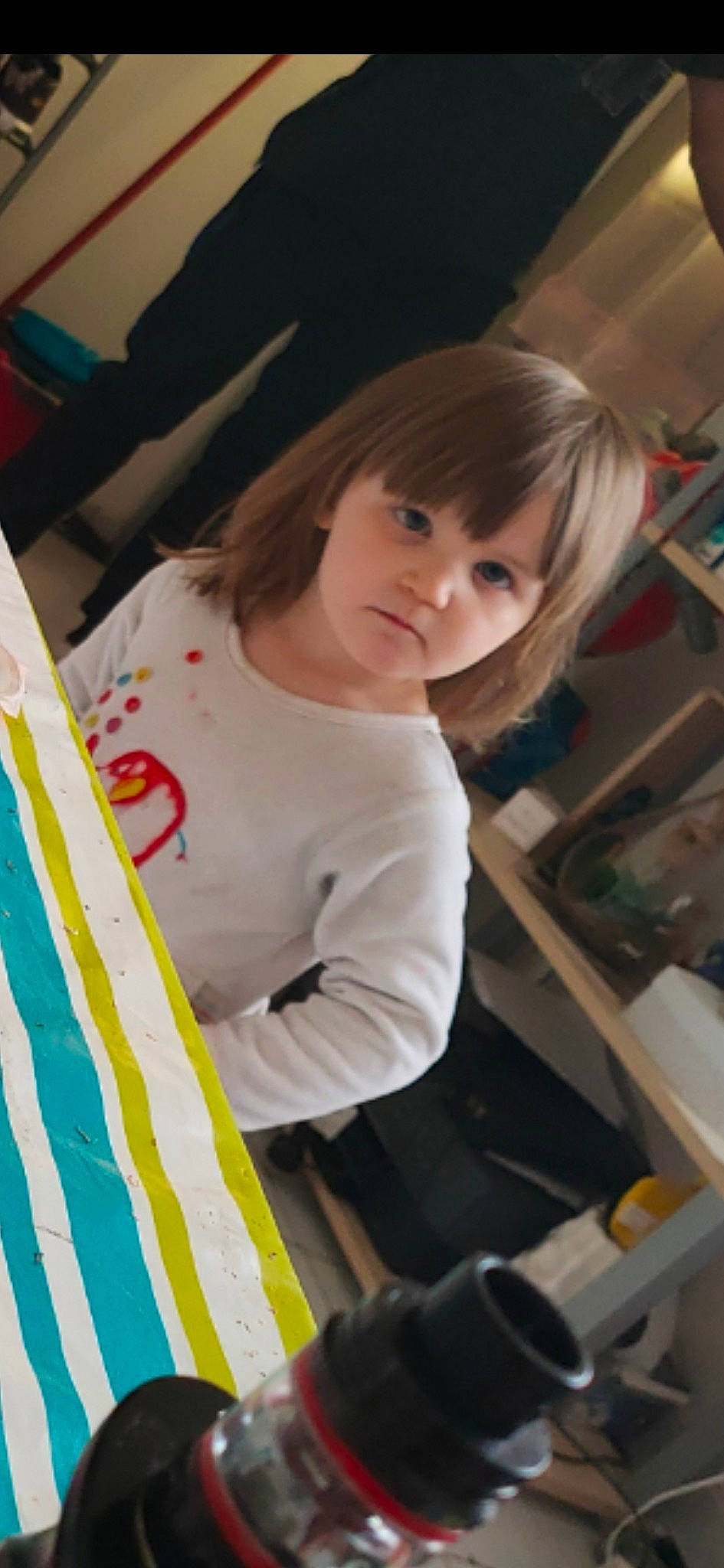 Liliana participe au concours pour gagner de l'argent avec cette photo : bangs, child, elbow, event, flooring, fun, hime_cut, human_leg, leisure, long_hair, person, play, recreation, room, shelf, sitting, sleeve, t_shirt, thigh, toddler