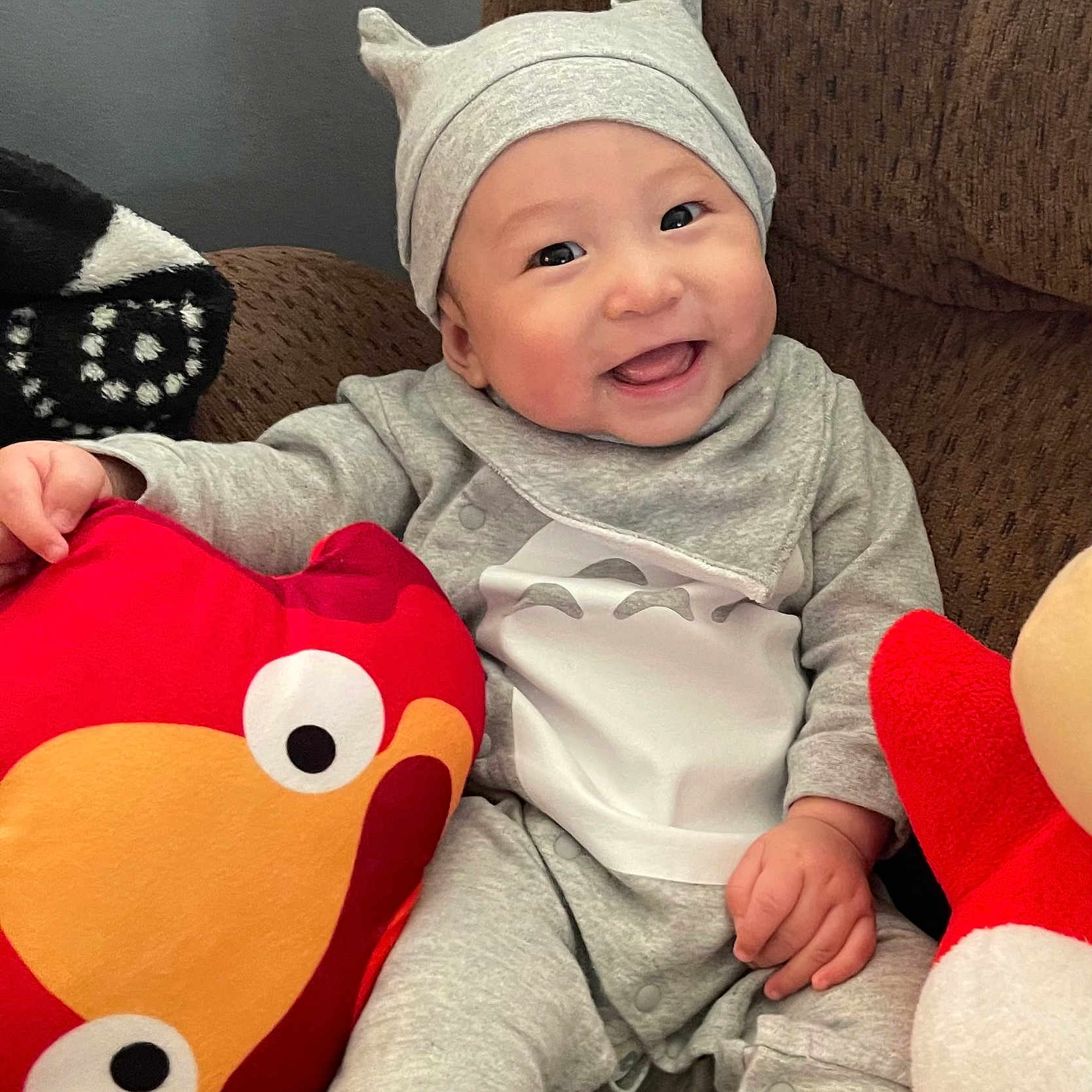 Su-Jin joined the competition — help win amazing prizes! baby, cheerful, child, couch, cozy, cute, eyes, face, gray_clothing, hand, happy, hat, home, indoor, infant, plush_toy, red_pillow, sitting, smiling, soft_toy