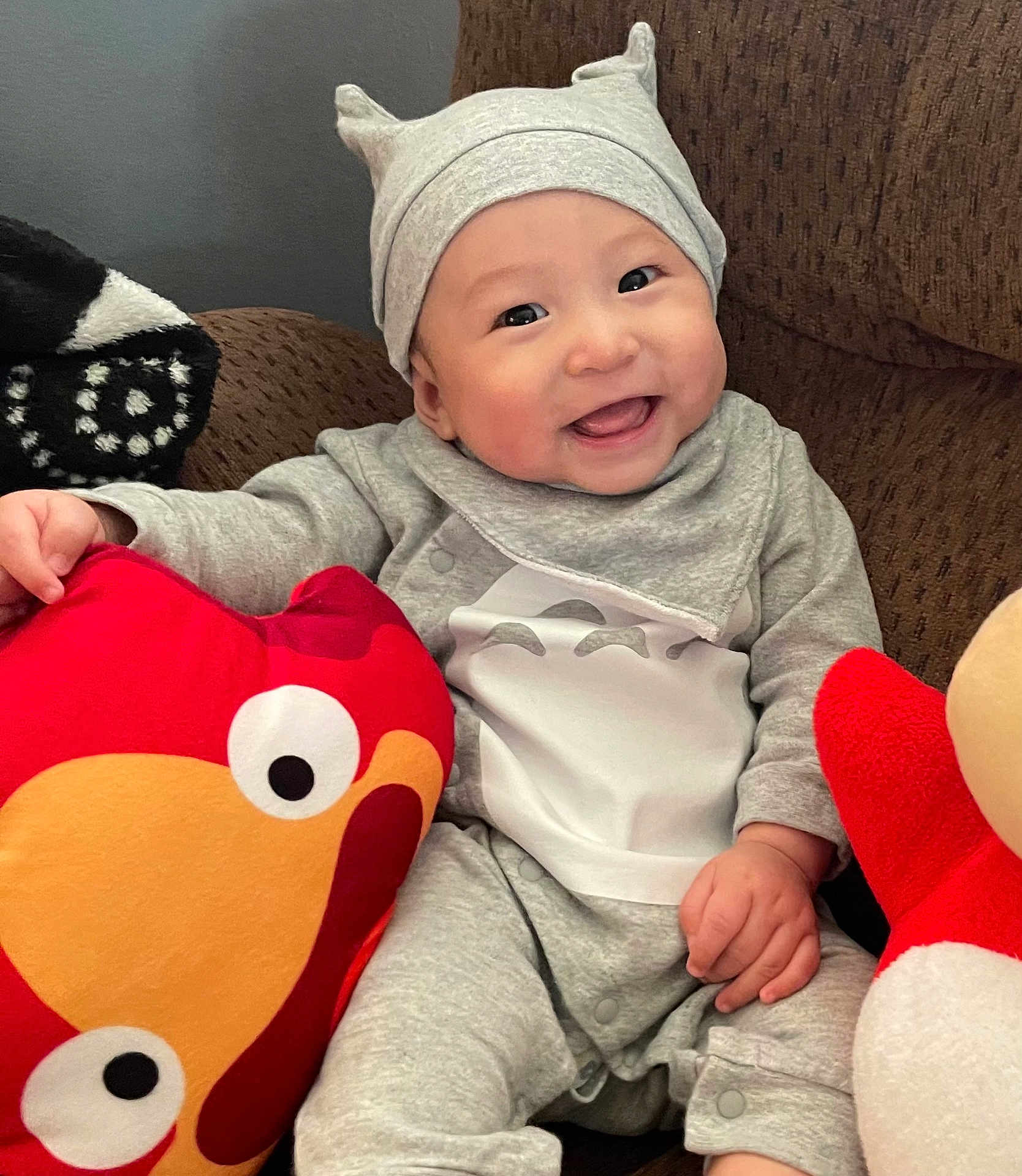 Su-Jin joined the competition — help win amazing prizes! baby, cheerful, child, couch, cozy, cute, eyes, face, gray_clothing, hand, happy, hat, home, indoor, infant, plush_toy, red_pillow, sitting, smiling, soft_toy