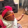 Honestii joined the competition — help win amazing prizes! baby, child, headband, flower, sunglasses, bib, indoor, person, infant, pink, clothing, patterned_pants, hand, face, cute, looking_sideways, furniture, soft_focus, living_room, curious