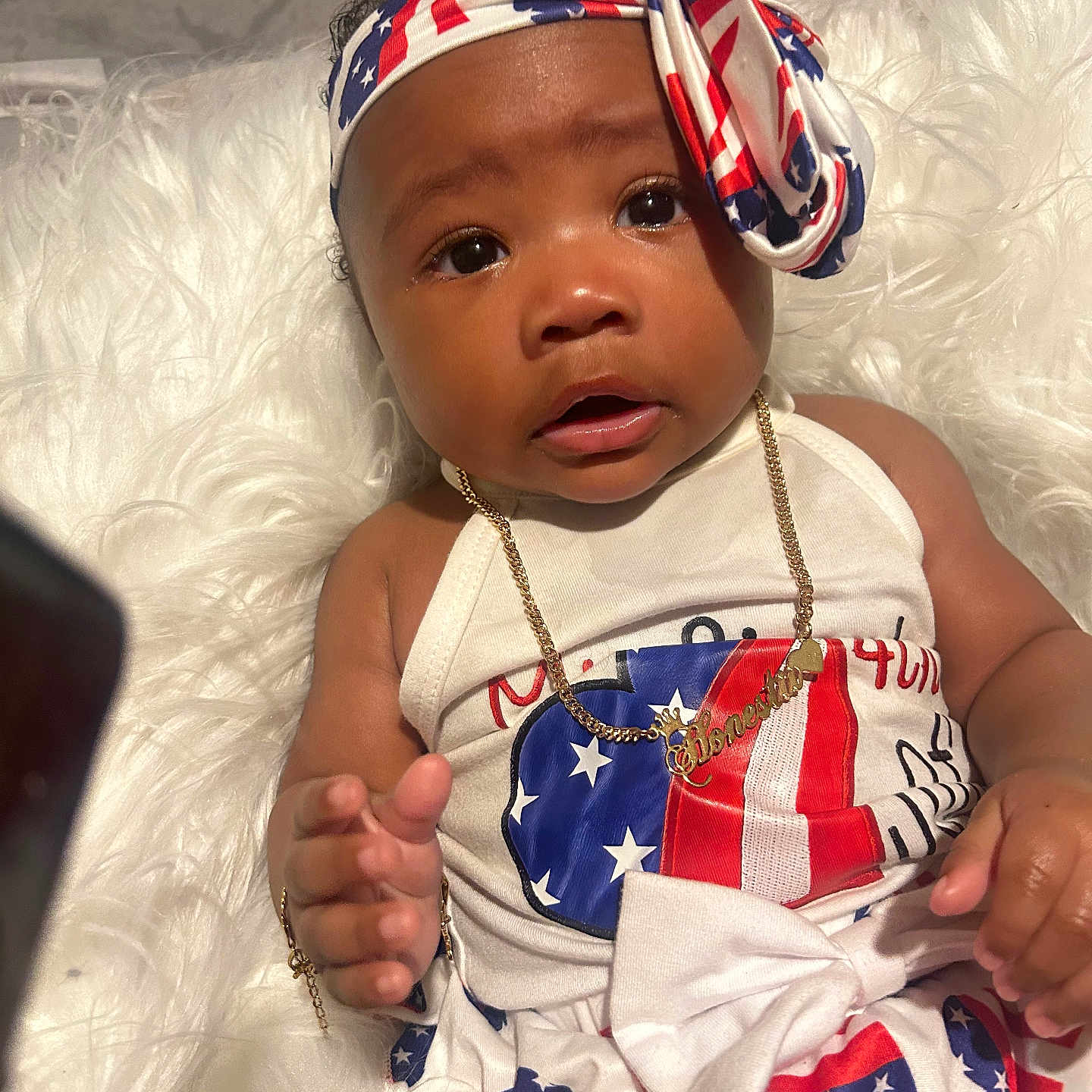 Honestii joined the competition — help win amazing prizes! baby, child, clothing, cute, expression, face, fur_texture, gold_bracelet, gold_necklace, hand, headband, indoor, infant, person, portrait, red_white_blue, sitting, stars, stripes, white_background