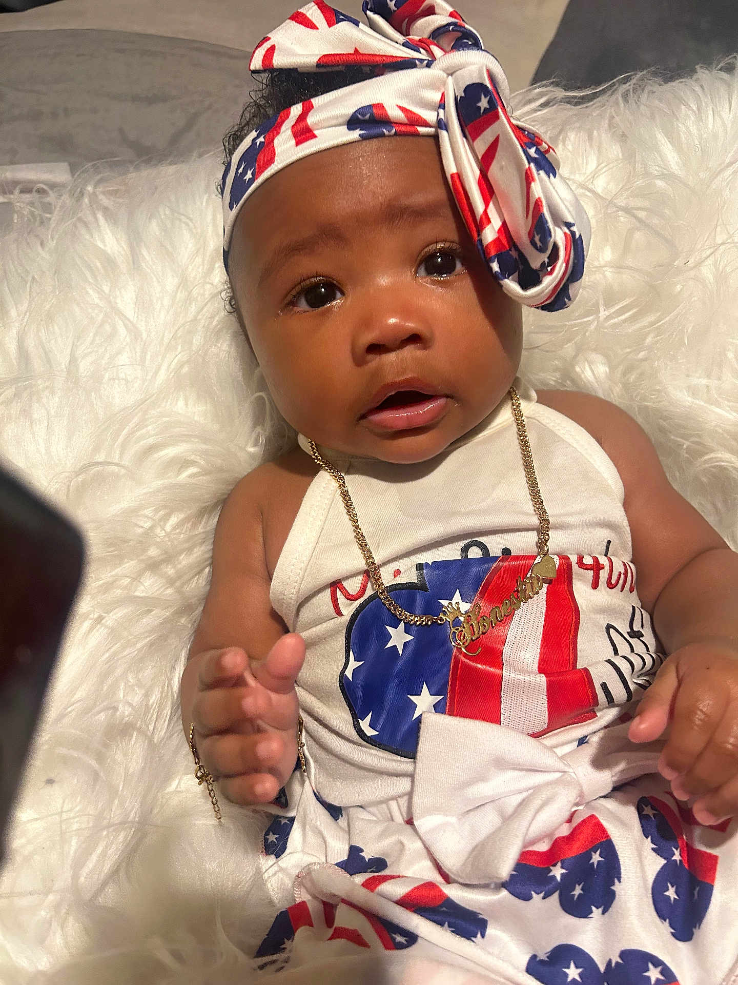 Honestii joined the competition — help win amazing prizes! baby, child, infant, headband, gold_necklace, gold_bracelet, clothing, red_white_blue, stars, stripes, white_background, fur_texture, portrait, cute, person, face, hand, sitting, expression, indoor