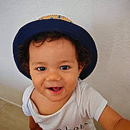 Azaël a rejoint le concours — aidez-le/la à gagner de superbes lots ! toddler, child, hat, smiling, curly_hair, white_shirt, happy, indoors, portrait, face, cute, baby, person, sitting, looking_up, joyful, casual, skin, eyes, expression