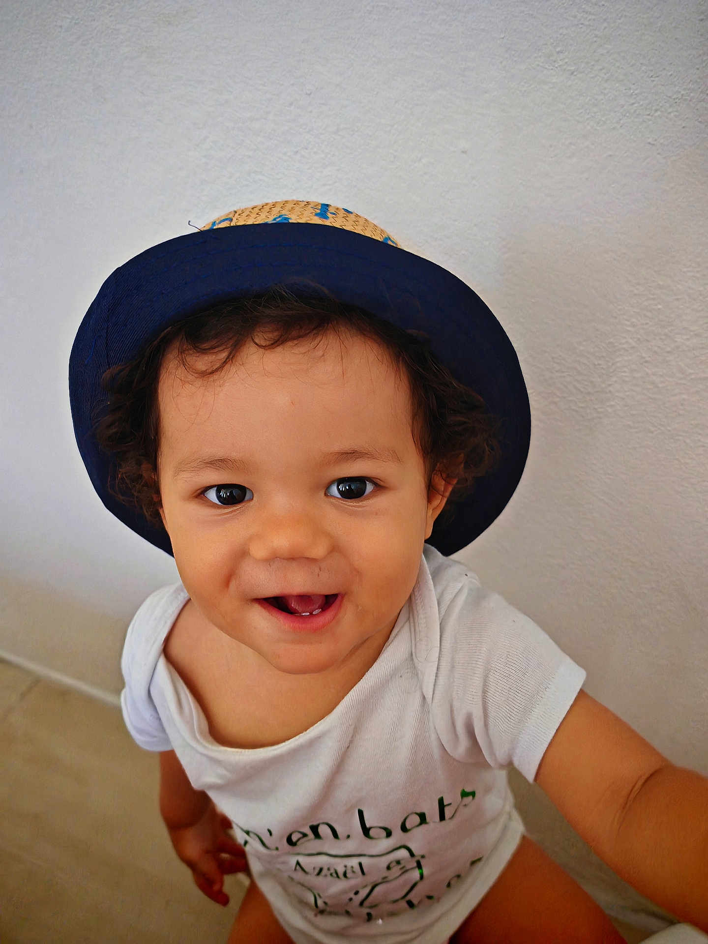 Azaël a rejoint le concours — aidez-le/la à gagner de superbes lots ! toddler, child, hat, smiling, curly_hair, white_shirt, happy, indoors, portrait, face, cute, baby, person, sitting, looking_up, joyful, casual, skin, eyes, expression