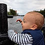 Fatah Juba participe au concours pour gagner de l'argent avec cette photo : toddler, child, striped_shirt, navy_vest, water, river, railing, outdoor, cloudy_sky, cityscape, profile, curious, smiling, baby, person, daytime, nature, young_child, side_view, casual_clothing