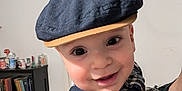 Fatah Juba participe au concours pour gagner de l'argent avec cette photo : baby, child, face, cap, hat, plaid_shirt, suspenders, smiling, indoor, person, hand, bookshelf, books, furniture, clothing, portrait, cute, happy, headwear, young