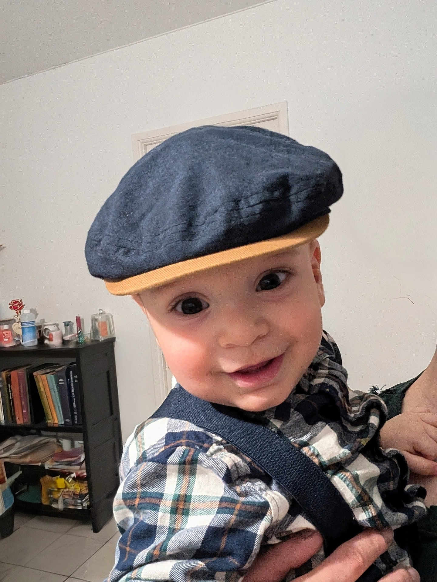 Fatah Juba participe au concours pour gagner de l'argent avec cette photo : baby, child, face, cap, hat, plaid_shirt, suspenders, smiling, indoor, person, hand, bookshelf, books, furniture, clothing, portrait, cute, happy, headwear, young
