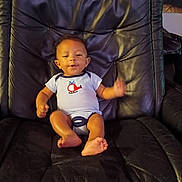 Anthony is registered to the contest to win money with this photo: baby, infant, child, portrait, sitting, recliner, chair, indoor, smiling, waving, face, eyes, clothing, bodysuit, bare_feet, furniture, photograph, home, dark_background, cute