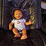 baby, infant, child, portrait, sitting, recliner, chair, indoor, smiling, waving, face, eyes, clothing, bodysuit, bare_feet, furniture, photograph, home, dark_background, cute