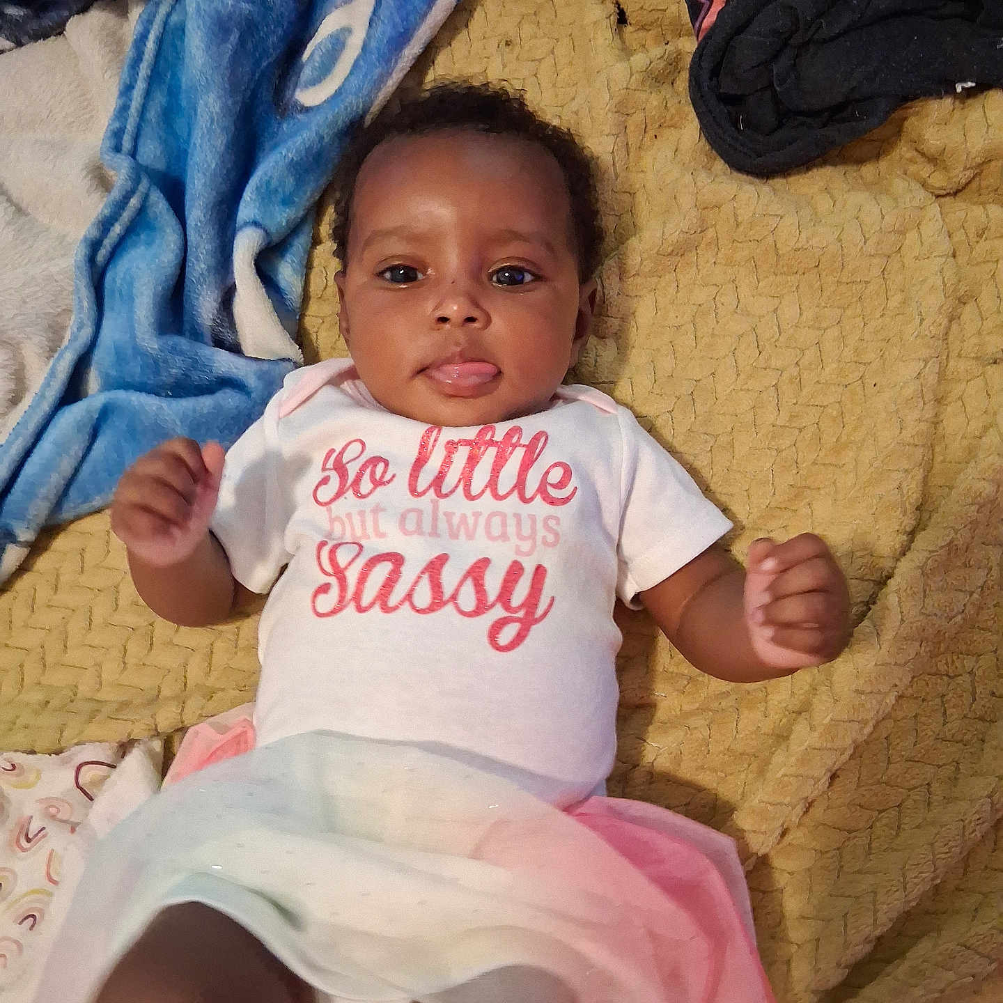 Rayna-Jean joined the competition — help win amazing prizes! baby, blanket, cheeky, child, clothing, colorful, cute, expression, fabric, face, indoors, infant, lying_down, person, playful, shirt, skirt, text, tongue_out, young_child