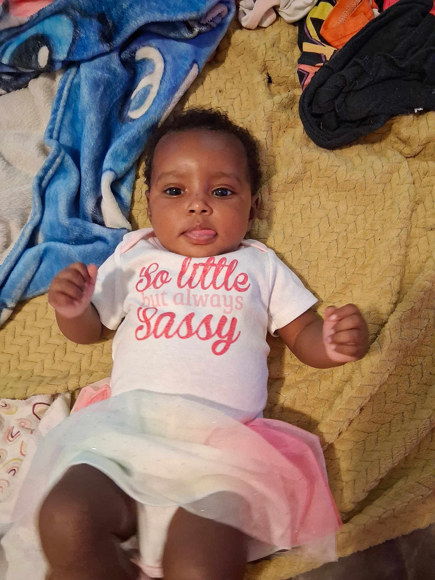 Rayna-Jean joined the competition — help win amazing prizes! baby, infant, child, clothing, shirt, skirt, blanket, text, tongue_out, cheeky, lying_down, fabric, colorful, cute, person, indoors, playful, expression, face, young_child