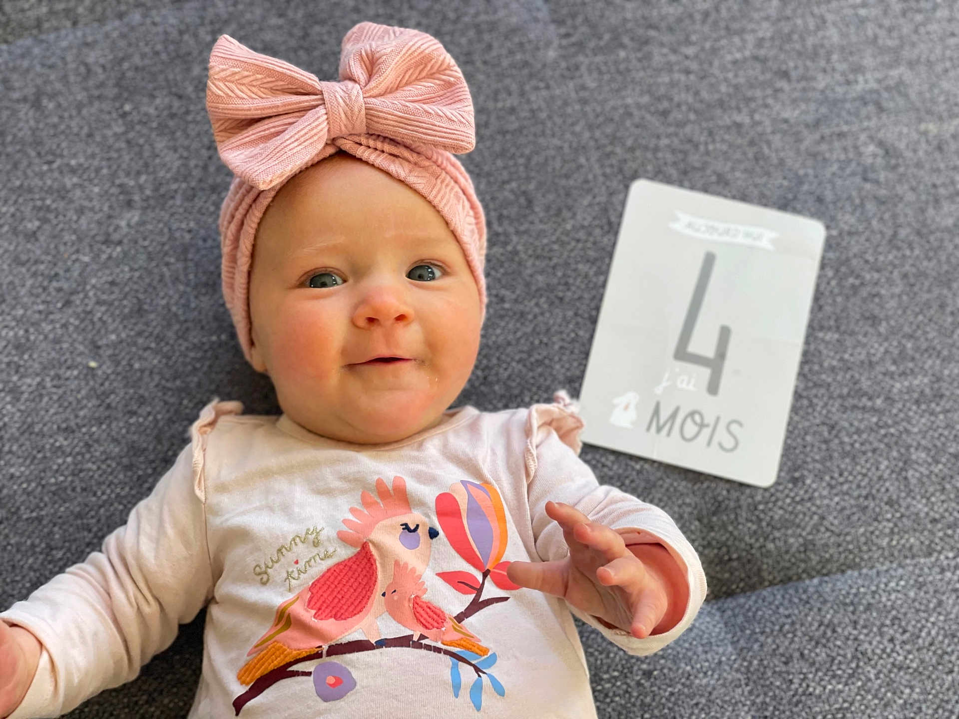 Alba participe au concours pour gagner de l'argent avec cette photo : baby, infant, headband, pink, bow, smile, face, clothing, milestone_card, text, laying, carpet, cute, child, person, young, milestone, four_months, apparel, indoors