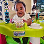 Jayden is registered to the contest to win money with this photo: baby, child, exersaucer, toy, smiling, indoor, person, playtime, happy, curly_hair, topknot, clothing, socks, furniture, living_room, television, window, curtain, decor, play_area