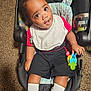 Jayden is registered to the contest to win money with this photo: baby, child, car_seat, toy, keys, red_shirt, black_shorts, white_socks, sneakers, carpet, indoor, cute, smiling, curious, infant, person, young_child, playful, seated, portrait