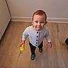 Tiago participe au concours pour gagner de l'argent avec cette photo : toddler, child, indoor, wooden_floor, toy, sweater, smiling, standing, looking_up, person, footwear, buttoned_cardigan, short_hair, home, flooring, cute, playful, baby, young_child, portrait
