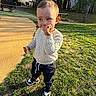 toddler, child, outdoor, grass, sweater, snack, sneakers, playground, daylight, trees, bench, person, park, young_child, casual_clothing, happy, standing, nature, sunlight, leisure