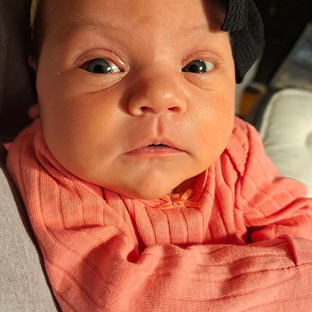 Xylena joined the competition — help win amazing prizes! apparel, baby, child, closeup, clothing, curious, cute, expression, face, headband, holding, indoors, infant, newborn, peach, person, portrait, ribbed, skin, wide_eyes