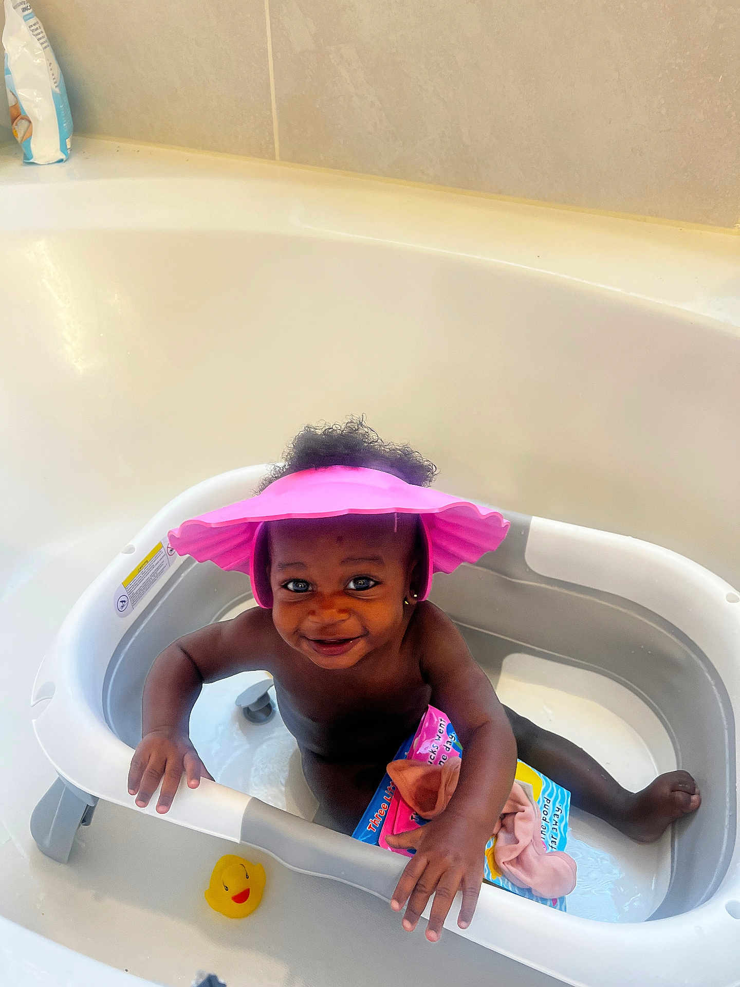Pearla joined the competition — help win amazing prizes! toddler, baby, bathtub, pink_hat, rubber_duck, bath_time, smiling, child, water, toy, book, indoor, happy, curly_hair, skin, playful, bathroom, cute, sitting, young_child