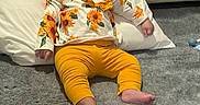 Valentina is registered to the contest to win money with this photo: baby, child, infant, yellow_leggings, flower_print, headband, pillow, carpet, floor, cute, indoors, resting, clothing, sitting, person, portrait, toddler, headwear, home, cozy