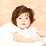 adorable, baby, blue_eyes, child, chubby_cheeks, closeup, curly_hair, cute, expression, face, floral_dress, indoors, infant, person, portrait, resting, skin, soft_light, white_blanket, young