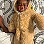 Amaree is registered to the contest to win money with this photo: baby, bear_costume, bedspread, child, cozy, cute, fabric, face, fuzzy_clothing, happy, indoor, infant, lying_down, onesie, pattern, person, playful, sleepwear, smiling, toy