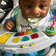 Amaree is registered to the contest to win money with this photo: baby, bib, blanket, blue_pajamas, child, close_up, colorful_toy, cute, face, hand, happy, indoor, infant, pacifier, person, playing, seat, soft, toy_piano, young_child