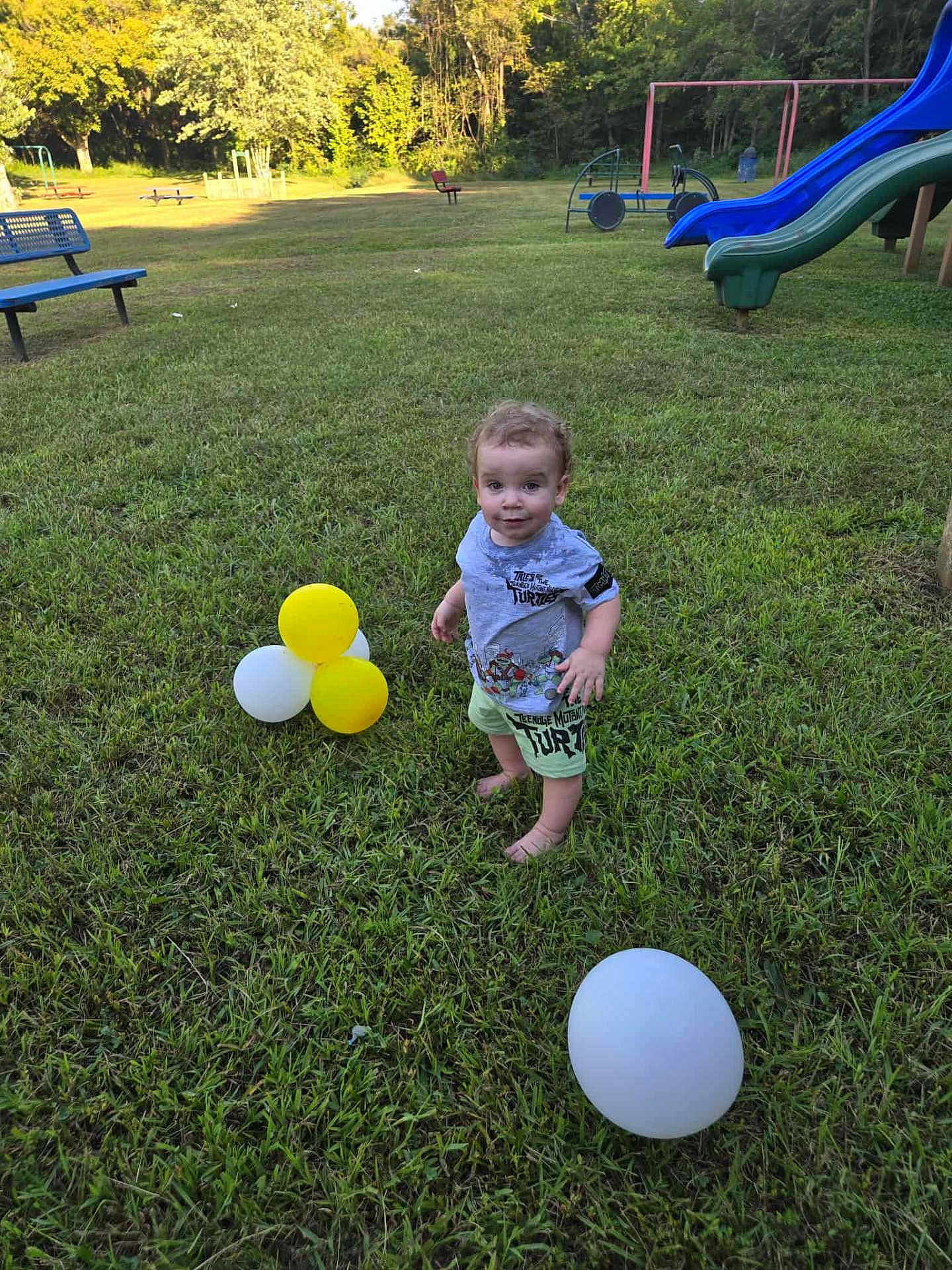 Kevin Goldston is registered to the contest to win money with this photo: toddler, child, grass, balloons, playground, slide, bench, outdoor, sunlight, trees, greenery, summer, nature, barefoot, smiling, cute, casual_clothing, park, fun, daytime