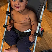 Kiyro is registered to the contest to win money with this photo: baby, baby_toddler, bare_chest, black_hair, child, comfort, cute, expression, footwear_absent, furry_rug, happy, home, indoor, infant, pants, person, seated, smiling, stroller, wooden_floor
