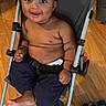 baby, baby_toddler, bare_chest, black_hair, child, comfort, cute, expression, footwear_absent, furry_rug, happy, home, indoor, infant, pants, person, seated, smiling, stroller, wooden_floor