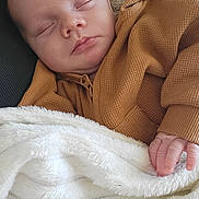 Sacha participe au concours pour gagner de l'argent avec cette photo : baby, sleeping, blanket, brown_clothing, pacifier, hand, face, cozy, infant, soft_texture, rest, peaceful, portrait, closeup, indoor, child, newborn, couch, relaxation, comfort