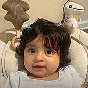 Yara is registered to the contest to win money with this photo: baby, child, infant, smile, face, hair_clip, white_clothing, plush_toy, dinosaur_toy, leaf_toy, cushion, seat, indoors, cute, portrait, young_child, person, soft_toys, happy, closeup