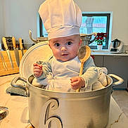 Lenny participe au concours pour gagner de l'argent avec cette photo : baby, infant, chef_hat, cooking_pot, wooden_spoon, kitchen, countertop, apron, cute, child, 6_months, utensils, window, plant, knife_block, expression, portrait, indoor, person, cooking