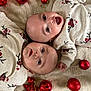 baby, infant, twin_babies, matching_clothes, reindeer_pajamas, christmas_ornaments, red_balls, red_star, holiday_theme, blanket, lying_down, cute, festive, smiling, happy, indoors, celebration, child, toddler, face