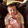 Eloise joined the competition — help win amazing prizes! baby, infant, pink_outfit, blanket, brown_blanket, indoor, furniture, fan, cabinet, wooden_furniture, curly_hair, person, young_child, portrait, seated, hand, face, home_interior, relaxed, soft_texture