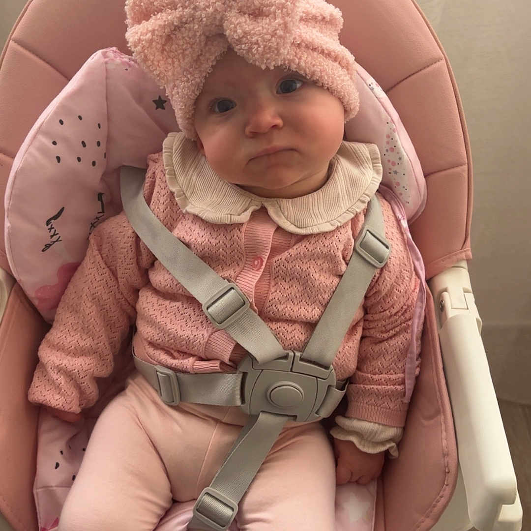 Elya a rejoint le concours — aidez-le/la à gagner de superbes lots ! baby, bow, child, clothing, cute, expression, face, floor, footwear, furniture, headband, high_chair, indoor, infant, pajamas, person, pink, sitting, soft_texture, straps