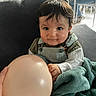 baby, balloon, blanket, couch, indoor, child, person, hand, smile, curly_hair, clothing, sitting, furniture, table, chair, floor, adult, casual, blanket_texture, soft_lighting