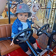 Haroun participe au concours pour gagner de l'argent avec cette photo : toddler, child, amusement_ride, steering_wheel, bucket_hat, denim_jacket, carousel, pig_statue, seat, playful, outdoor, daylight, funfair, cute, expression, toy_car, seatbelt, person, hat, footwear