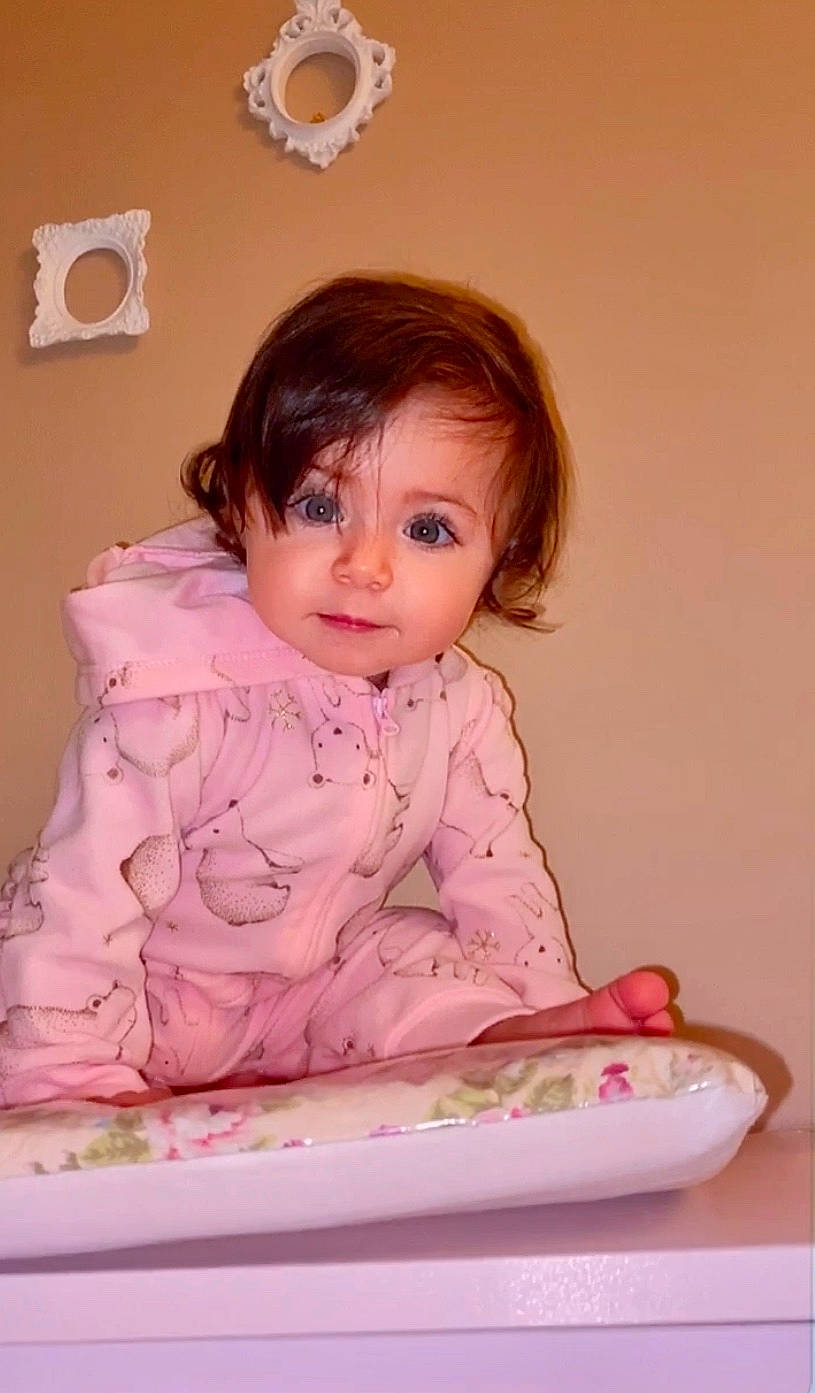 Rebecca is registered to the contest to win money with this photo: baby, baby_toddler_clothing, cheek, child, dress, face, fun, hairstyle, happy, iris, linens, lip, magenta, person, pink, room, sitting, skin, sleeve, standing