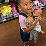 child, girl, smiling, laughing, toy_store, dolls, baby_dolls, hello_kitty, shopping, portrait, standing, pink_clothing, hair_bow, ponytail, sandals, shelves, retail, colorful, indoors, happy