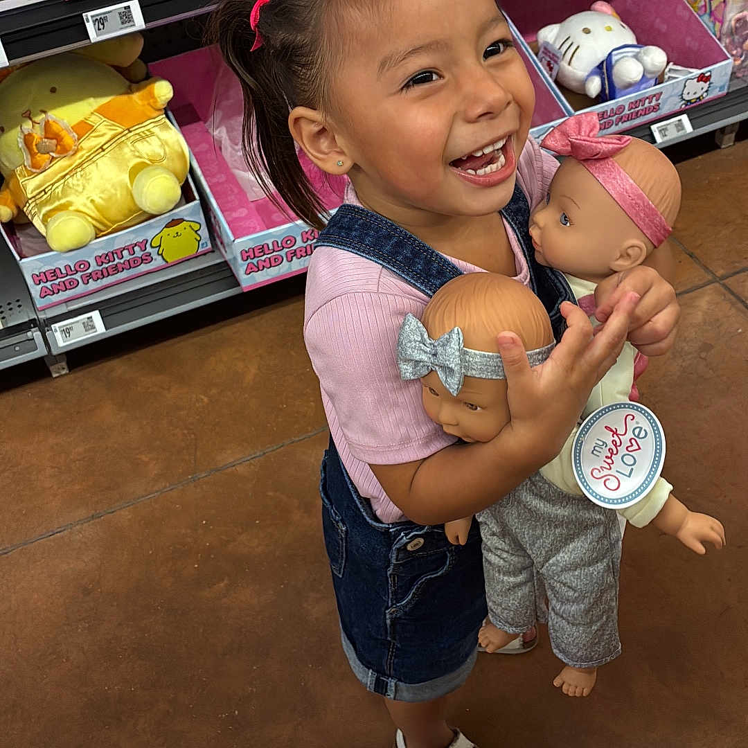 Nicole is registered to the contest to win money with this photo: child, girl, smiling, laughing, toy_store, dolls, baby_dolls, hello_kitty, shopping, portrait, standing, pink_clothing, hair_bow, ponytail, sandals, shelves, retail, colorful, indoors, happy