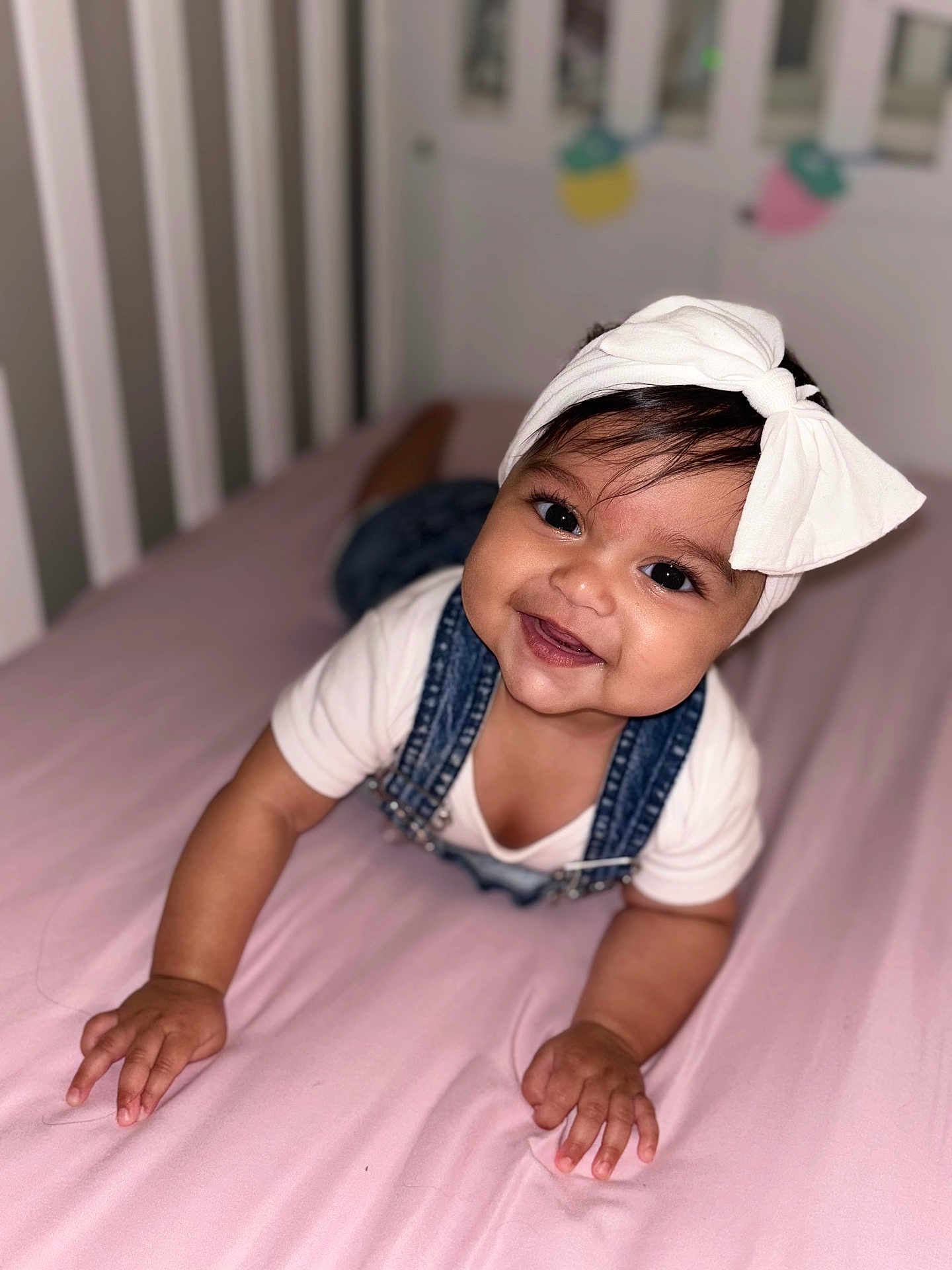 Haley Alish joined the competition — help win amazing prizes! baby, child, smile, headband, bow, denim, overalls, pink_bed, crib, crawling, happy, cute, infant, indoors, portrait, person, baby_clothes, baby_skin, baby_hands, baby_face