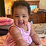 Anjayah is registered to the contest to win money with this photo: baby, child, smiling, sitting, pink_dress, curly_hair, bed, blanket, furniture, lamp, wooden_dresser, indoors, happy, cheerful, person, portrait, cute, infant, room, cozy