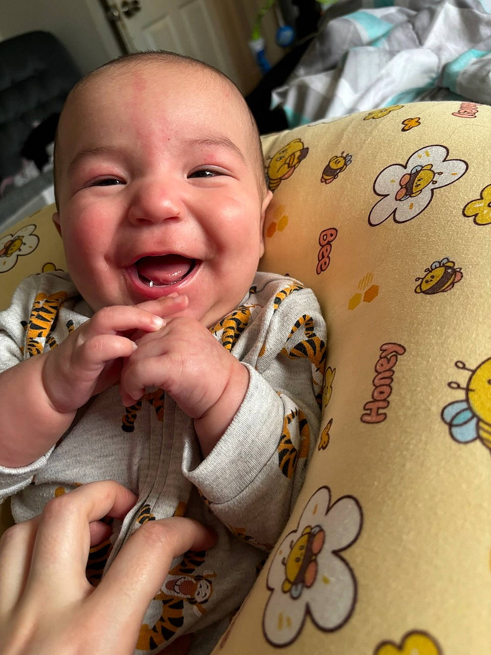baby, bee_pattern, candid, child, closeup, clothing, cozy, cute, expression, face, hands, happy, indoor, infant, nursery, onesie, person, pillow, smiling, tiger_pattern