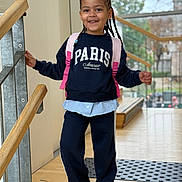 Brianna a rejoint le concours — aidez-le/la à gagner de superbes lots ! child, smiling, braided_hair, backpack, sweatshirt, indoor, railing, wooden_floor, window, natural_light, casual_clothing, happy, person, portrait, young, standing, fashion, footwear, school, ready