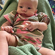 Alice is registered to the contest to win money with this photo: baby, infant, child, blanket, clothing, onesie, camouflage, indoor, person, face, skin, hand, foot, comfort, soft, green, relaxed, cute, expression, portrait