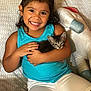 Potato is registered to the contest to win money with this photo: child, smiling, kitten, cat, couch, plush_toy, horse_plush, blue_tank_top, white_shorts, happy, indoor, cute, hugging, young_child, dark_hair, patterned_couch, toy, pet, cozy, portrait