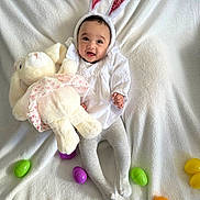 Noeli is registered to the contest to win money with this photo: baby, bunny_ears, plush_toy, stuffed_animal, easter_eggs, white_blanket, tights, smiling, cute, child, holiday, costume, infant, indoors, celebration, soft_toy, happy, playful, festive, portrait