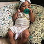 baby, infant, pacifier, headband, bow, onesie, patterned_pillow, floral_pattern, bird_pattern, striped_clothing, relaxing, indoors, cute, child, person, skin, legs, feet, hands, face