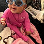 baby, child, pink_clothing, sunglasses, indoor, blanket, happy, smiling, person, face, head, seated, toy, cozy, nike_logo, polka_dots, newspaper, floor, cute, portrait